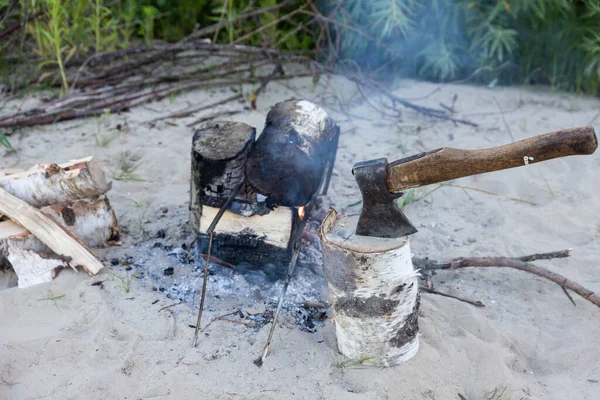 The ax sticks out in the tree against the fire.