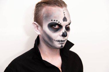 Duygularını göstermek için cadılar bayramı kafatası makyajı yapan siyah tişörtlü bir adamın portresi. Cadılar Bayramı partisi ya da korku teması. Meksika kültürü.