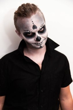 Duygularını göstermek için cadılar bayramı kafatası makyajı yapan siyah tişörtlü bir adamın portresi. Cadılar Bayramı partisi ya da korku teması. Meksika kültürü.