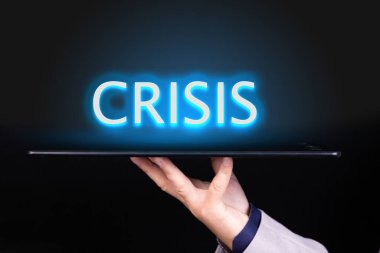 İnsan eli üzerinde neon bir metin yazan bir tablet tutar, CRISIS kelimesi. İş konsepti.