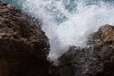 Taşlı bir sahilde dalgalar kırılır ve büyük bir püskürtme oluşur.