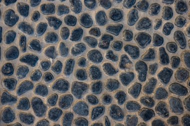 Beton yolda siyah çakıl taşı. Üst görünüm taşı arka planı. Deniz kenarındaki çakıl taşı fotoğraf dokusu. Taş kaldırım yüzeyi. Doğal dış dekorasyon malzemesi yuvarlanmış kaldırımlar