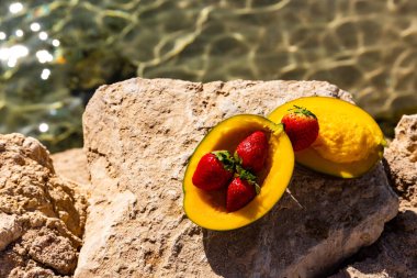 Olgun mango ve çilekler denize karşı bir taşın üzerinde yatıyor.