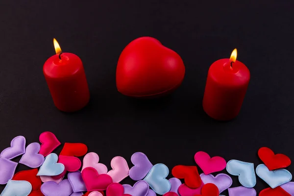 A lot of little hearts and two candles on a black background