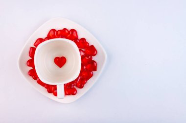 Beyaz arka planda, kalp şeklinde şekerlerle dolu beyaz bir fincan kahve. Sevgililer Günü