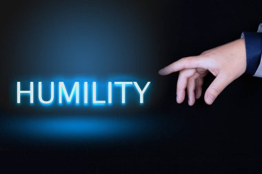 HUMILITY metin, bir kişinin işaret parmağıyla işaret edilen siyah arkaplan üzerinde neon harflerle yazılmış bir kelimedir..