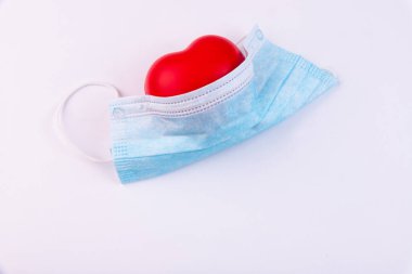 Kırmızı kalp ve tıbbi maske beyaz arka planda yatar. Sağlık, kardiyoloji ve medya kavramı.