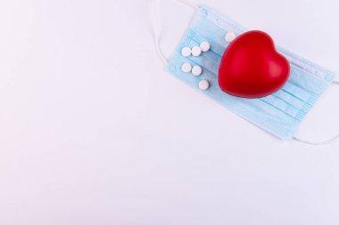 Kırmızı kalp, haplar ve tıbbi maske beyaz arka planda yatıyor. Sağlık, kardiyoloji ve medya kavramı.
