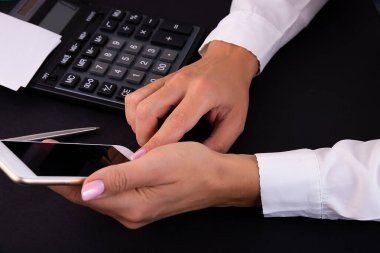Kadın akıllı telefon düğmesine basıyor. Arka planda, hesap makinesi siyah bir tabloda. Dijital aygıt kullanan kadın.