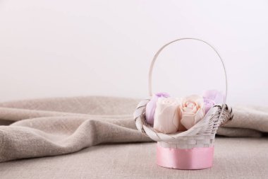 Menekşe ve bej renkli pastel güller keten bir masa örtüsünün üzerinde beyaz bir sepetin içinde..