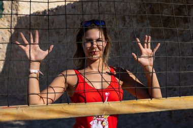 Kırmızı mayo giymiş genç bir kız voleybol sahasında akrobatik elementler sergiliyor. Kumda voleybol. Yoga.