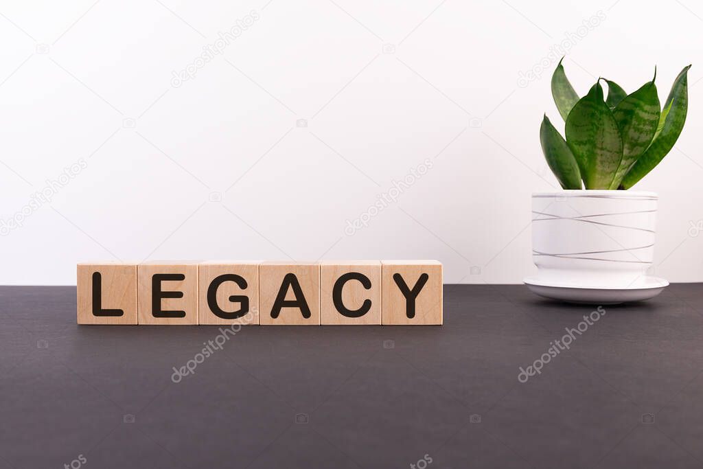 Legacy word on wooden cubes on a dark table with a flower and a light background