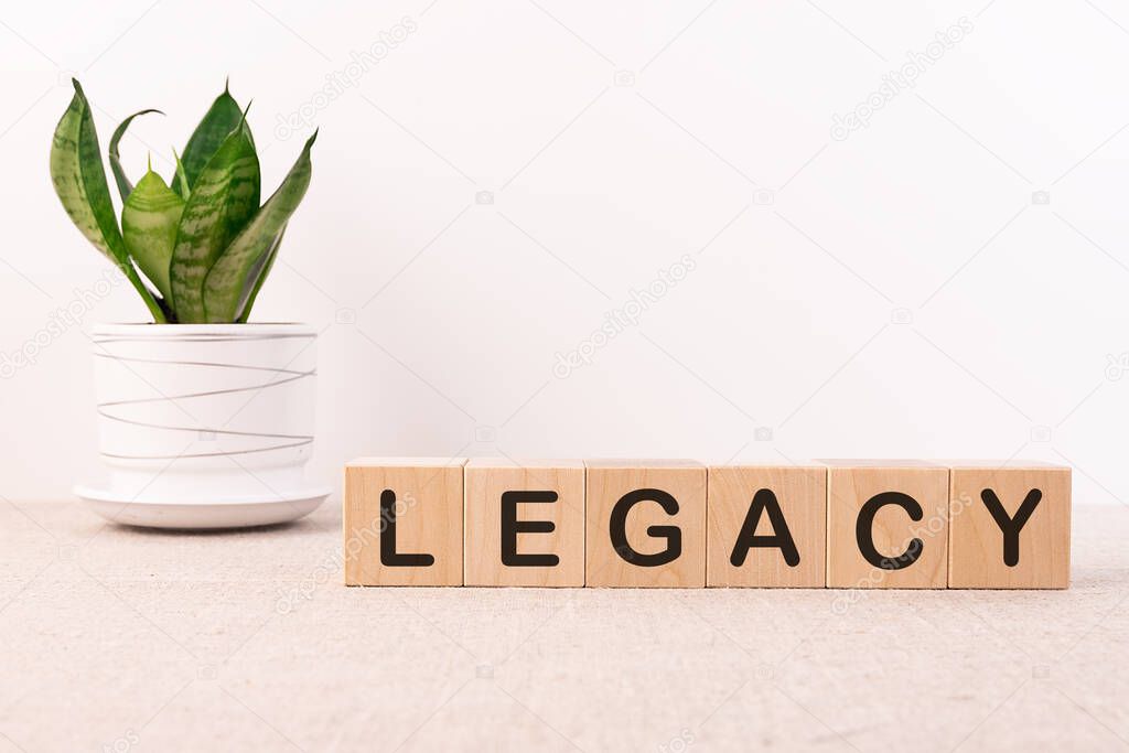 Legacy word on wooden cubes on a dark table with a flower and a light background