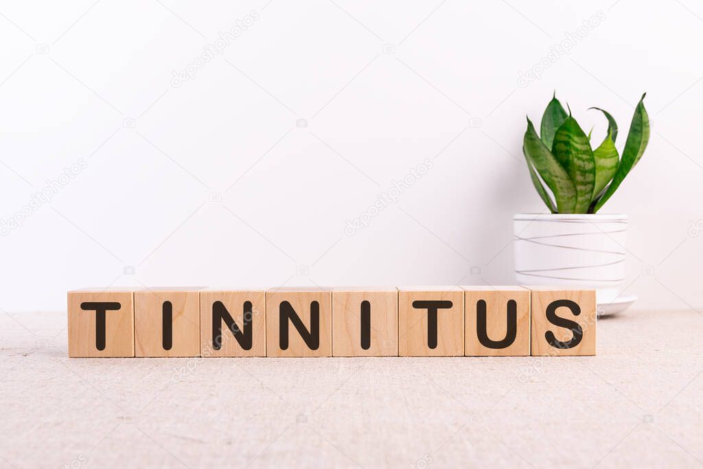 TINNITUS word concept written on wooden blocks, cubes on a light table with flower and light background