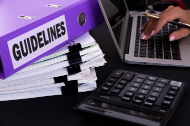 Üzerinde Kelime Kılavuzu yazan dizin, karanlık bir ofis masasında dizüstü bilgisayarlı, kalemli, hesap makineli ve raporlu.
