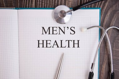 Stetoskop ve kalemle dolu bir masanın üzerinde MENS HEALTH yazılı defter sayfası, tıbbi konsept.