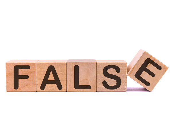 Word FALSE is made of wooden building blocks lying on the table and on a light background. Concept.