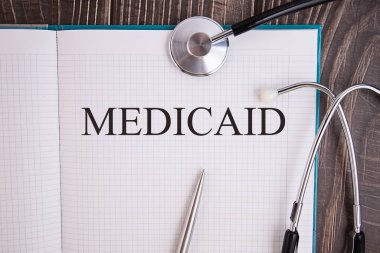 Metin MEDICAID içeren defter sayfası, steteskop ve kalem ile bir masanın üzerinde, tıbbi konsept.