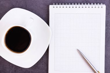 Ofis malzemeleri, defter, kalem, çiçek, karanlık arka planda bardaklar olan iş masası. Düz dizayn, yukarıdan görüş. Kavram.