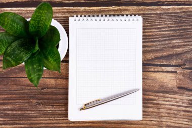 Not defteri, kalem, çiçek, tahta arka planda bardaklar olan iş masası. Düz tasarım, üst manzara. Kavram.