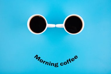 Mavi arka planda gülüşü olan iki beyaz kahve fincanı Sabah Kahvesi. Mutlu kahve fincanları..