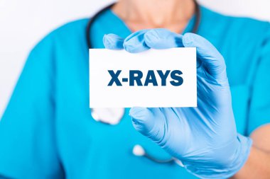 Mavi üniformalı bir doktor üzerinde X-RAYS yazan bir teşhis kartı tutuyor. Tıbbi konsept.