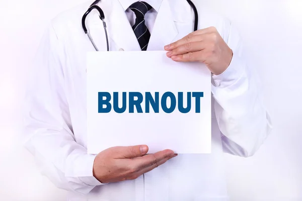 A doctor in medical clothing is holding a card with a diagnosis in front of him, text BURNOUT Medical concept.