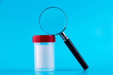 Steril şeffaf boş plastik analiz kabı ve büyüteç. Biyomateryal için kırmızı kapaklı steril tıbbi kap. Mavi bir arkaplanda izole edilmiş.