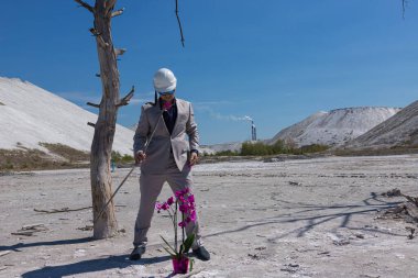 Endüstriyel bölgenin arka planında beyaz koruyucu başlıklı bir iş adamı bir orkide çiçeğini korur. Ekolojik çevre koruma kavramı. Ekolojik felaket.