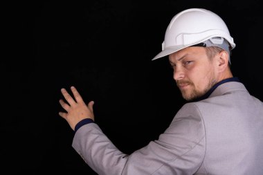 Beyaz kasklı mühendis siyah arka planda düşünceli bir şekilde duruyor.