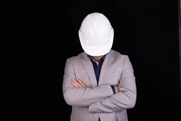 白いヘルメットのエンジニアは彼の頭を傾け 黒の背景に立っている — ストック写真