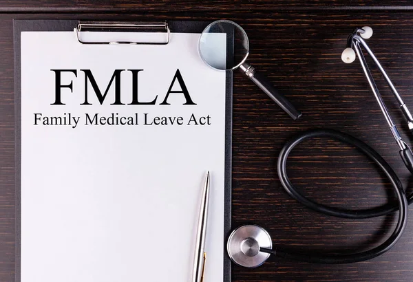 FMLA metni karanlık bir masada steteskop ve büyüteçle duran bir tablete yazılmıştır. Tıbbi konsept.
