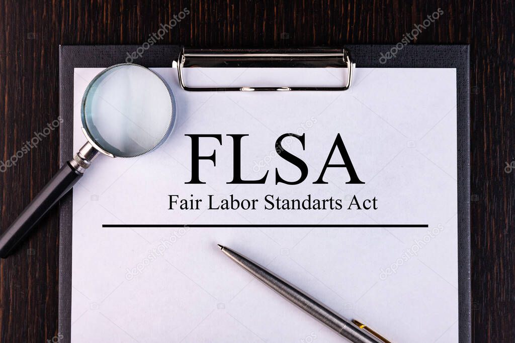 Text FLSA is written on a notebook with a pen and a magnifying glass lying on the table. Business concept.