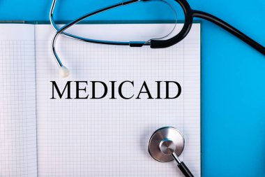 Masa ve steteskop üzerinde duran bir not defterine yazılmış MEDICAID metni. Tıbbi konsept.