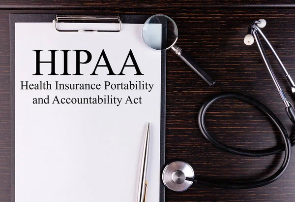 HIPAA metni karanlık bir masada steteskop ve büyüteçle duran bir tablete yazılmıştır. Tıbbi konsept.