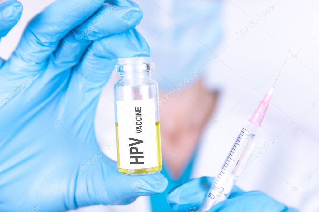 Text HPV VACCINE of is written on a bottle with the background of a doctor with a syringe in a medical glove and mask. Medical concept.