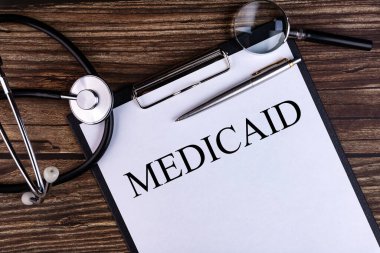 Masa ve steteskop üzerinde duran bir not defterine yazılmış MEDICAID metni. Tıbbi konsept.