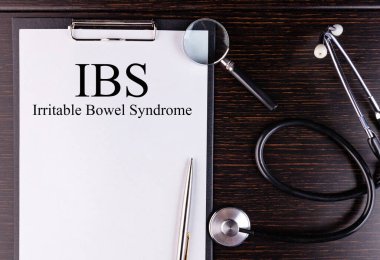 Masanın üzerinde duran bir not defterine ve steteskopa yazılmış IBS metni. Tıbbi konsept.