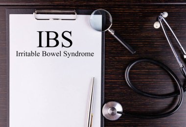 IBS text written in a notebook lying on a desk and a stethoscope. Medical concept. clipart