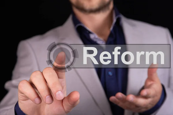 Businessman on a black background pressing a REFORM concept button.