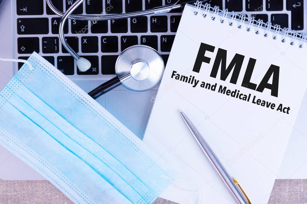 FMLA Family Medical Leave Act, the text is written in a notebook, next to a pen, a disposable medical mask and a laptop on a linen background.