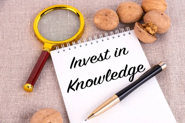 知識に投資 テキストはノートブックに書かれています ペンの横に リネンの背景に虫眼鏡とクルミ — ストック写真