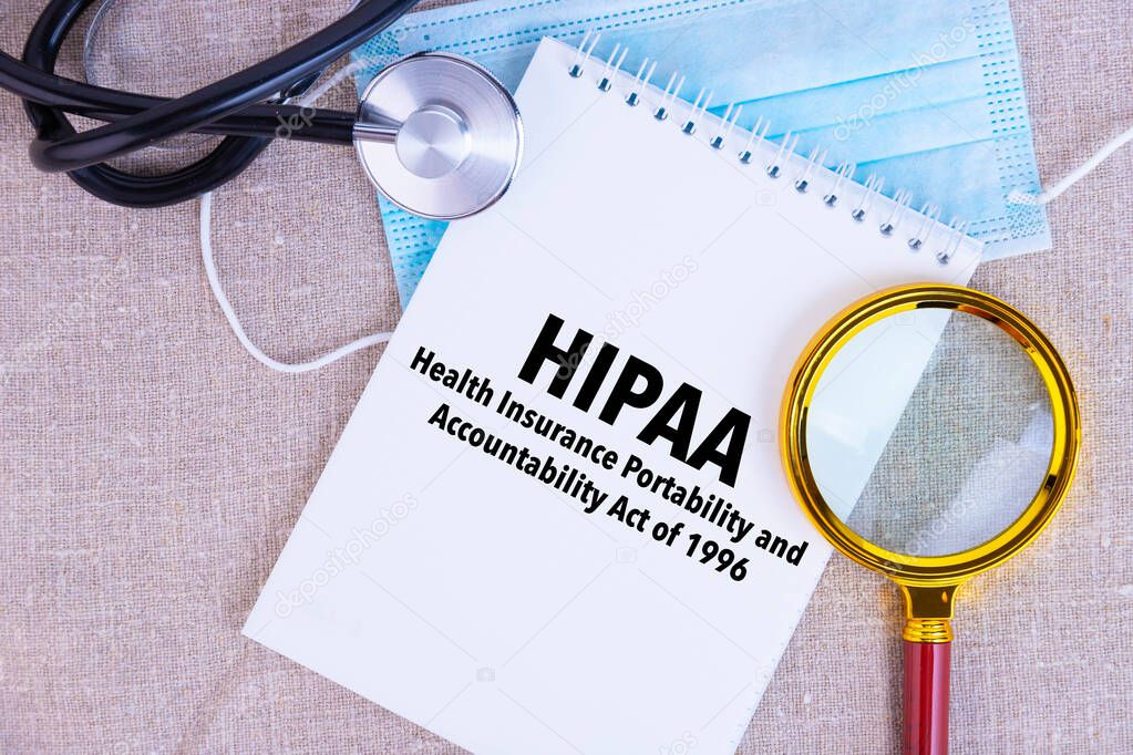 HIPAA, the Health Insurance Portability and Accountability Act of 1996, text written on white notepad, medical mask, stethoscope, magnifying glass on linen background.