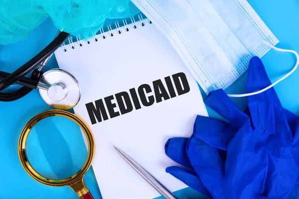 Mediicaid 文字写在笔记本上 蓝色背景 带听诊器和医疗面罩 医疗概念 — 图库照片