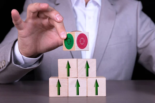 Growth or business concept. Arrow icon on wooden cubes and target, target, on wooden cubes on the background of a businessman in a gray suit sitting at the table.