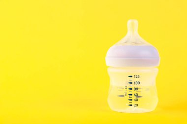 Süt için bir şişe su ve sarı arka planda bir emzik. Boşluğu kopyala.