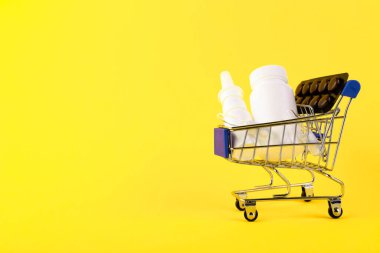 Boş mini alışveriş arabası, alışveriş arabası, sarı arka planda ilaçlarla dolu alışveriş sepeti. RFI bilgi talep ediyor. Boşluğu kopyala