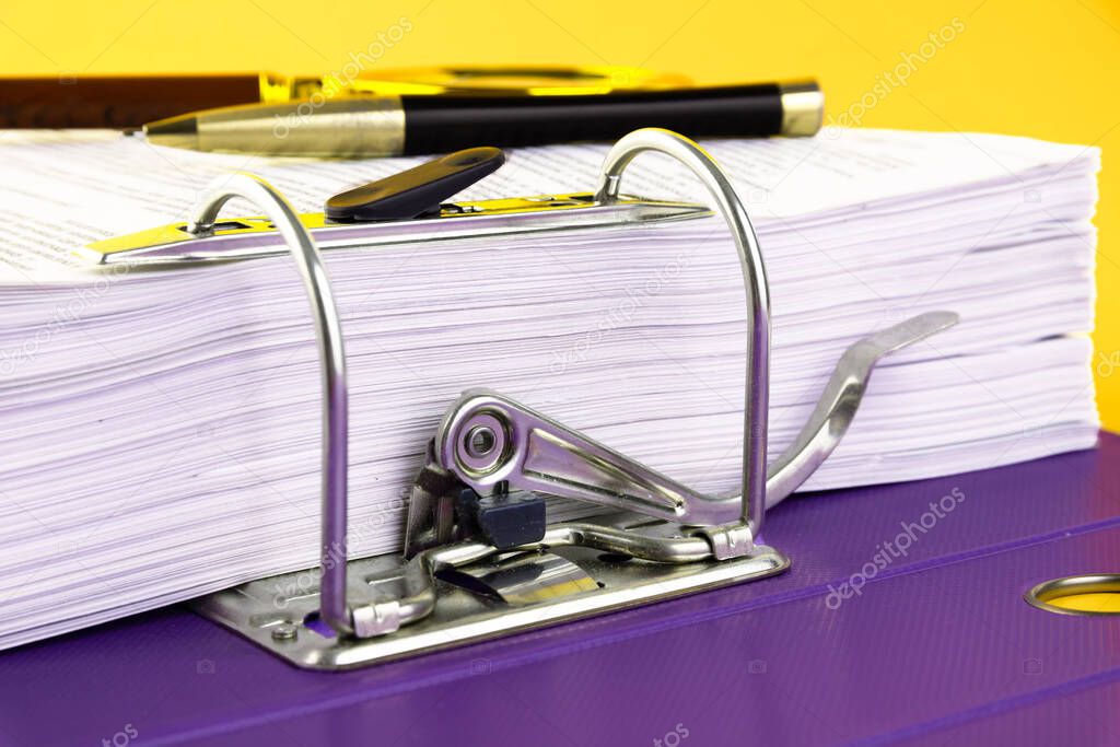 Close up of a pile of unfinished documents awaiting verification, a magnifying glass, on a yellow background. Business and education concept. Copy space