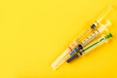 Parlak sarı arka planda tek kullanımlık şırıngalar. Grip ve koronavirüse karşı aşı. Sağlık sigortası konsepti. Tıbbi enjeksiyon. İğne, dozaj ölçeği. Düz yatıyordu. Kopyalama alanı olan üst görünüm.