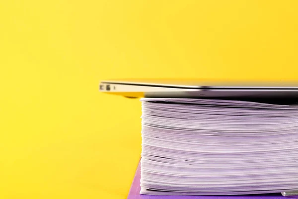 Office, folder with documents awaiting verification, laptop on a yellow background. Business and education concept. Copy space. Selective focus.